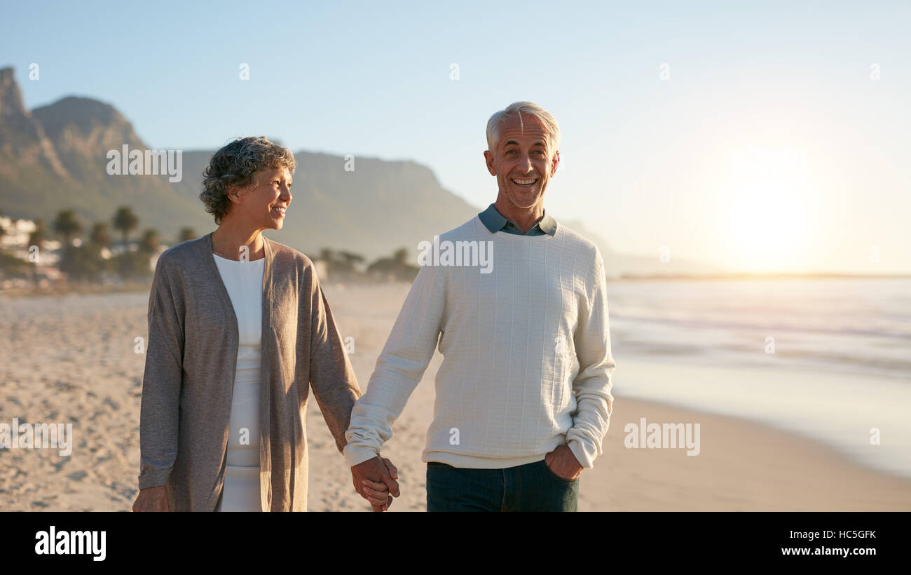 Outdoors shot of happy mature couple strolling on the beach. Senior man and senior woman taking a walk on the sea shore. Stock Photo