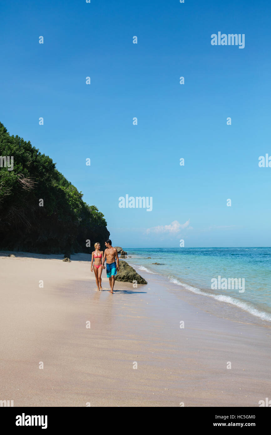 Shot of young man and woman walking on the tropical coast. Young couple strolling on the beach, enjoying summer vacation. Stock Photo