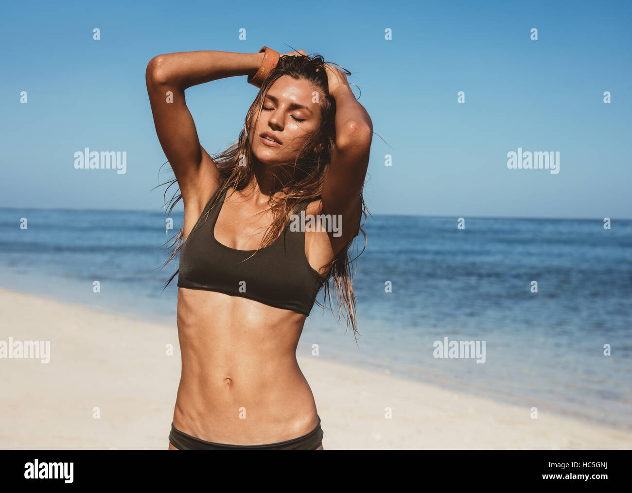 Portrait of sensuous female model in bikini standing on the beach. Sexy young woman posing in swimsuit on the sea shore. Stock Photo
