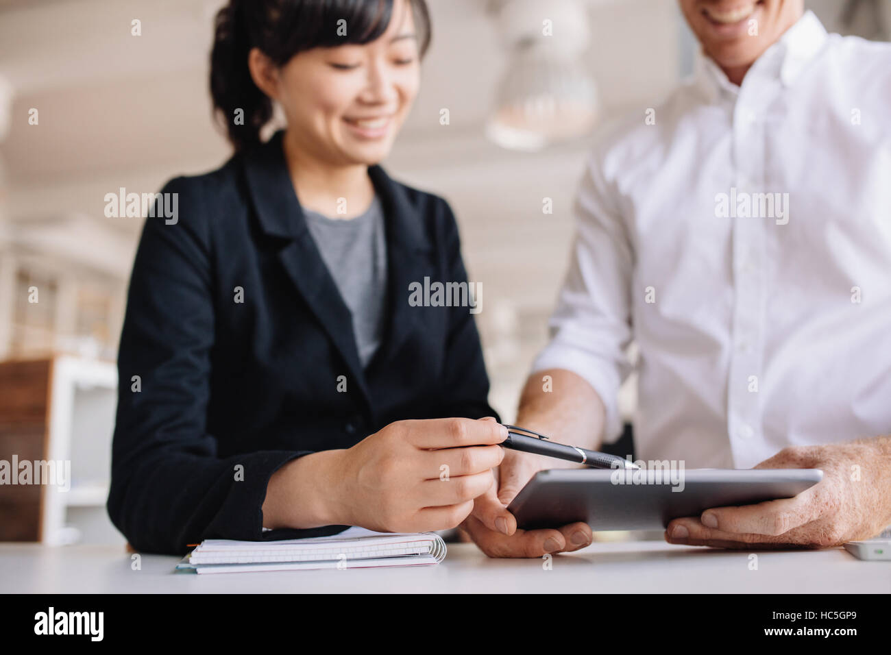 Two young business people working together, with female executive pointing digital tablet. Businessman and businesswoman using touchscreen computer in Stock Photo