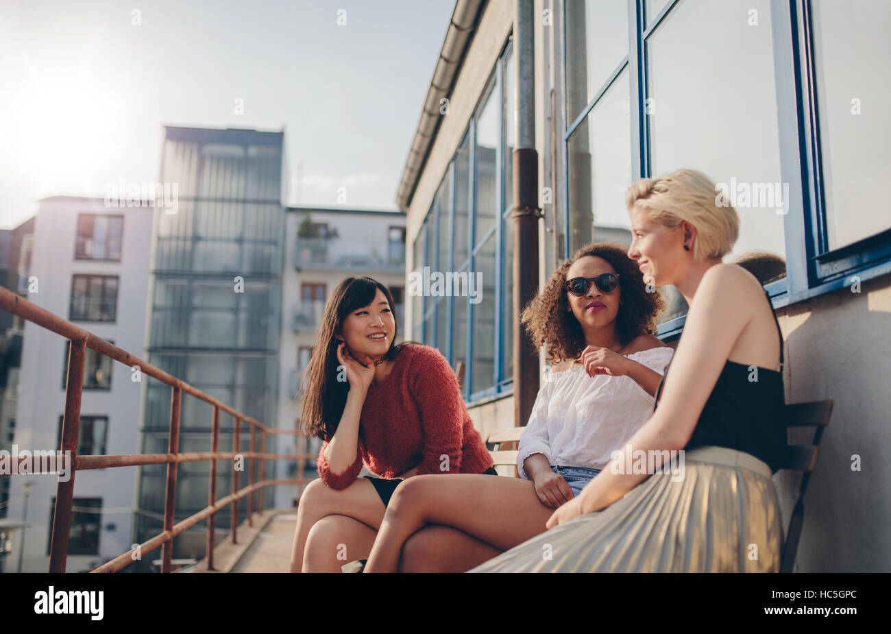 Three young female friends sitting in balcony. Women relaxing outdoors and chatting. Stock Photo
