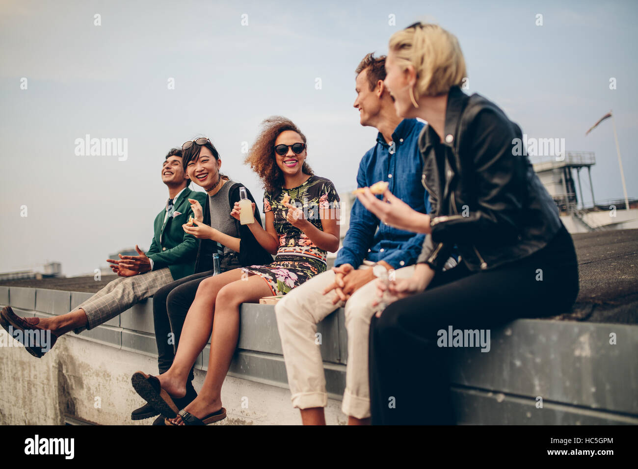 Happy young people partying on roof with drinks. Multiracial men and woman enjoying on terrace. Stock Photo