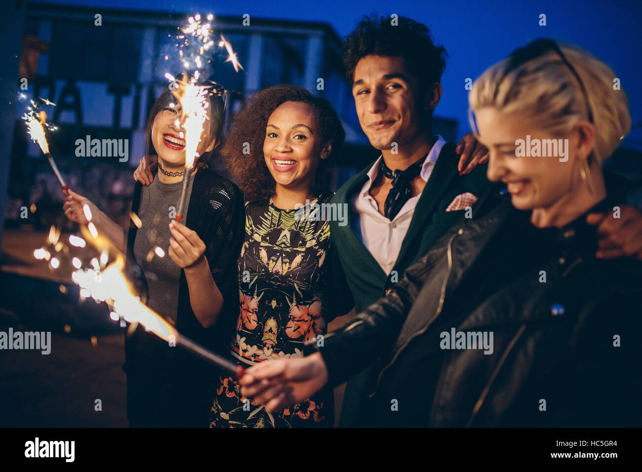 Shot of young friends at night with fireworks enjoying party. Group of friends with sparklers on road in evening. Stock Photo