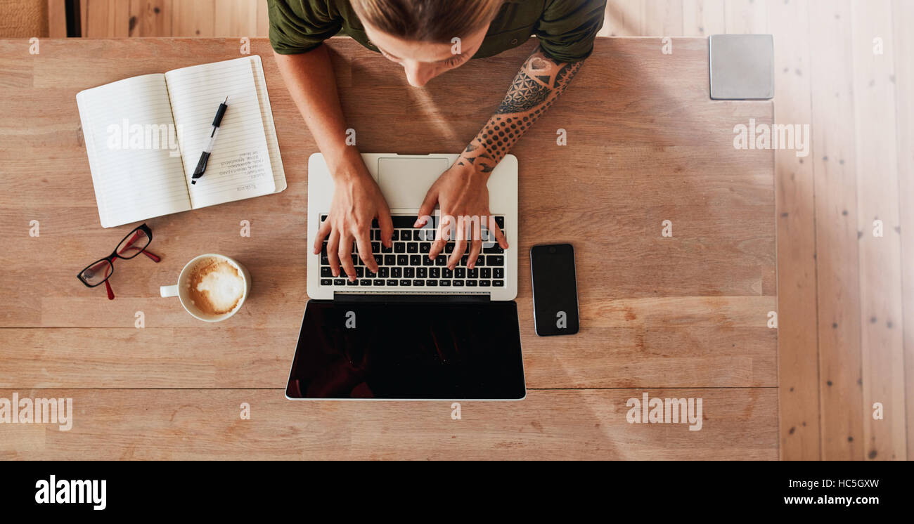 Top view of woman hands typing on laptop. Female sitting at cafe table with laptop, mobile phone, diary, coffee cup and glasses. Stock Photo