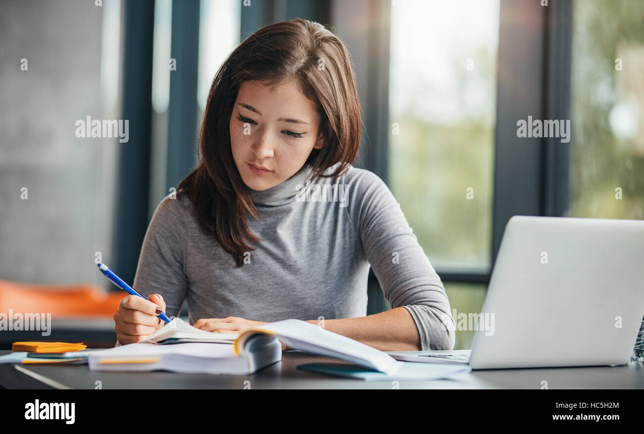 Shot of young woman taking down notes in diary. Female university student preparing note for the exam at library. Stock Photo