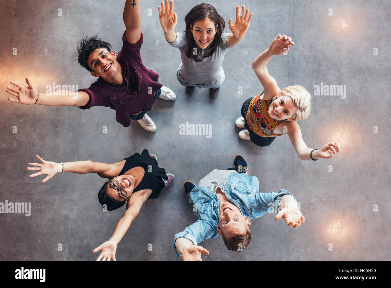 Top view of young students standing together looking up at camera with their hands raised in celebration. Stock Photo