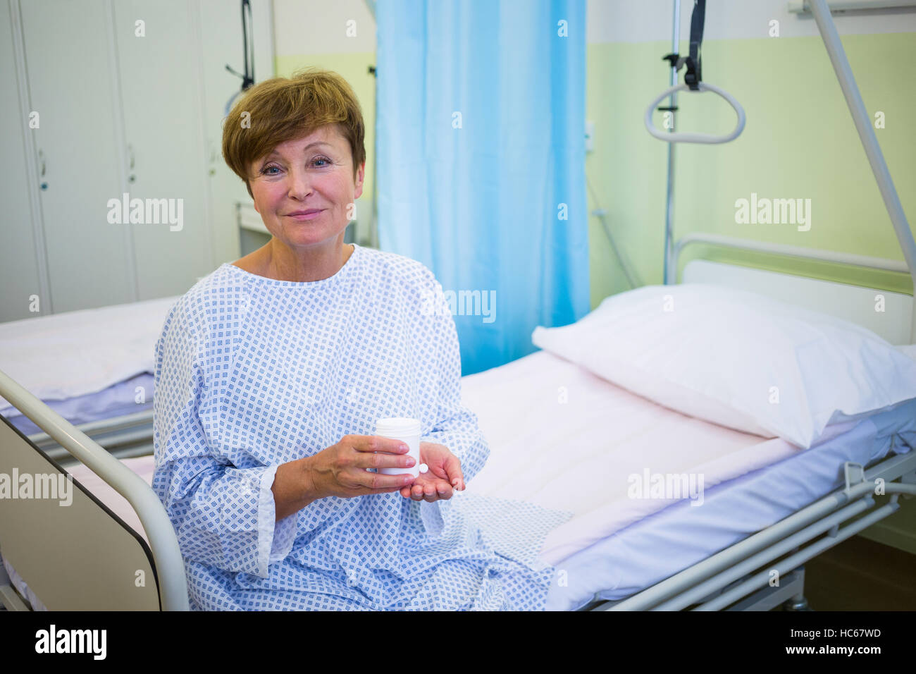 Portrait of senior patient sitting on a bed holding medicine Stock Photo