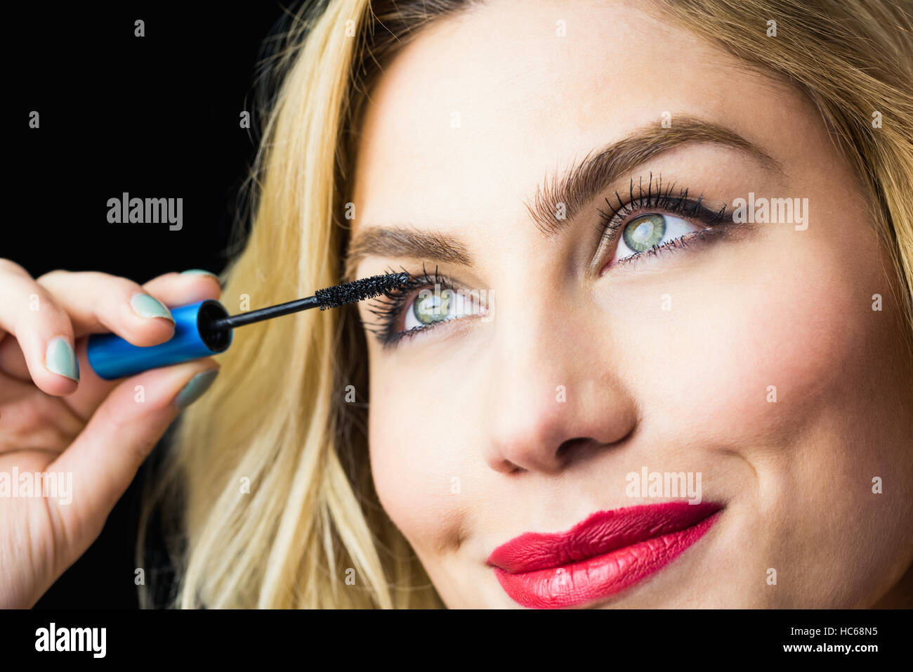 Beautiful woman applying mascara on eyelashes against black background Stock Photo