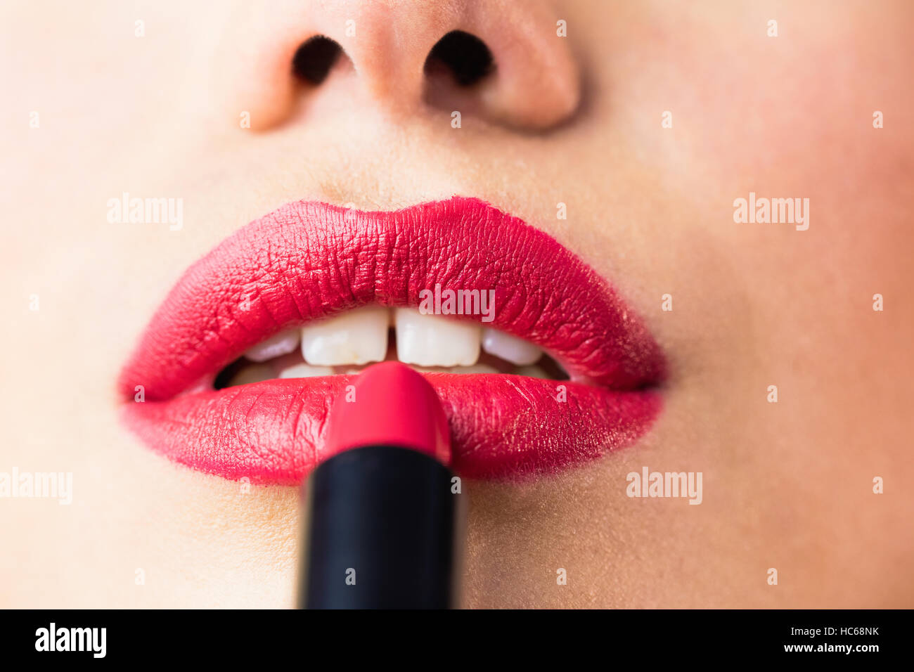 Beautiful woman applying red lipstick on lips against black background Stock Photo