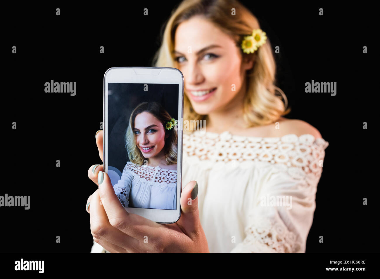 Beautiful woman clicking photo from mobile phone against black background Stock Photo