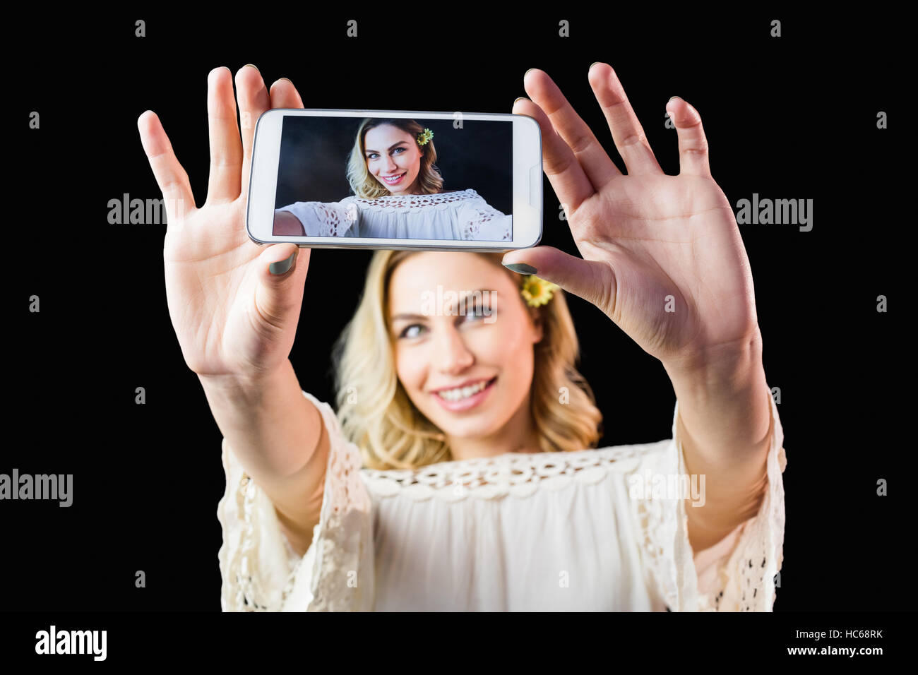 Smiling woman clicking photo from mobile phone against black background Stock Photo