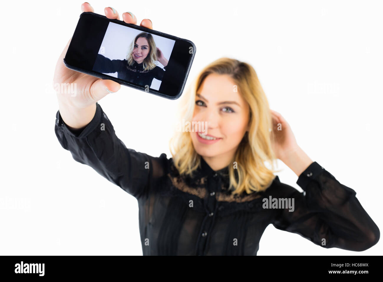 Smiling woman clicking photo from mobile phone against white background Stock Photo