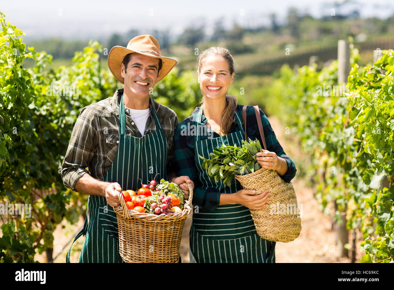 Portrait of happy farmer couple holding baskets of vegetables Stock Photo