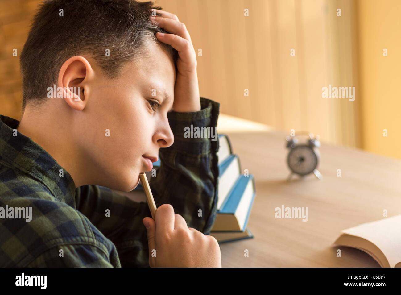 Young Boy Thinking Over a Book on Desk at Home Stock Photo