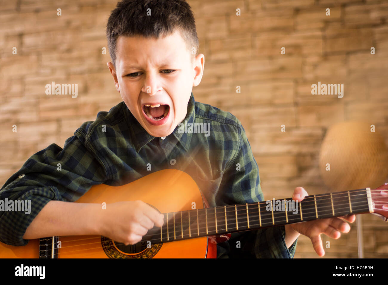Young Boy Singing Out Loud While Playing Acoustic Guitar in Living Room Stock Photo