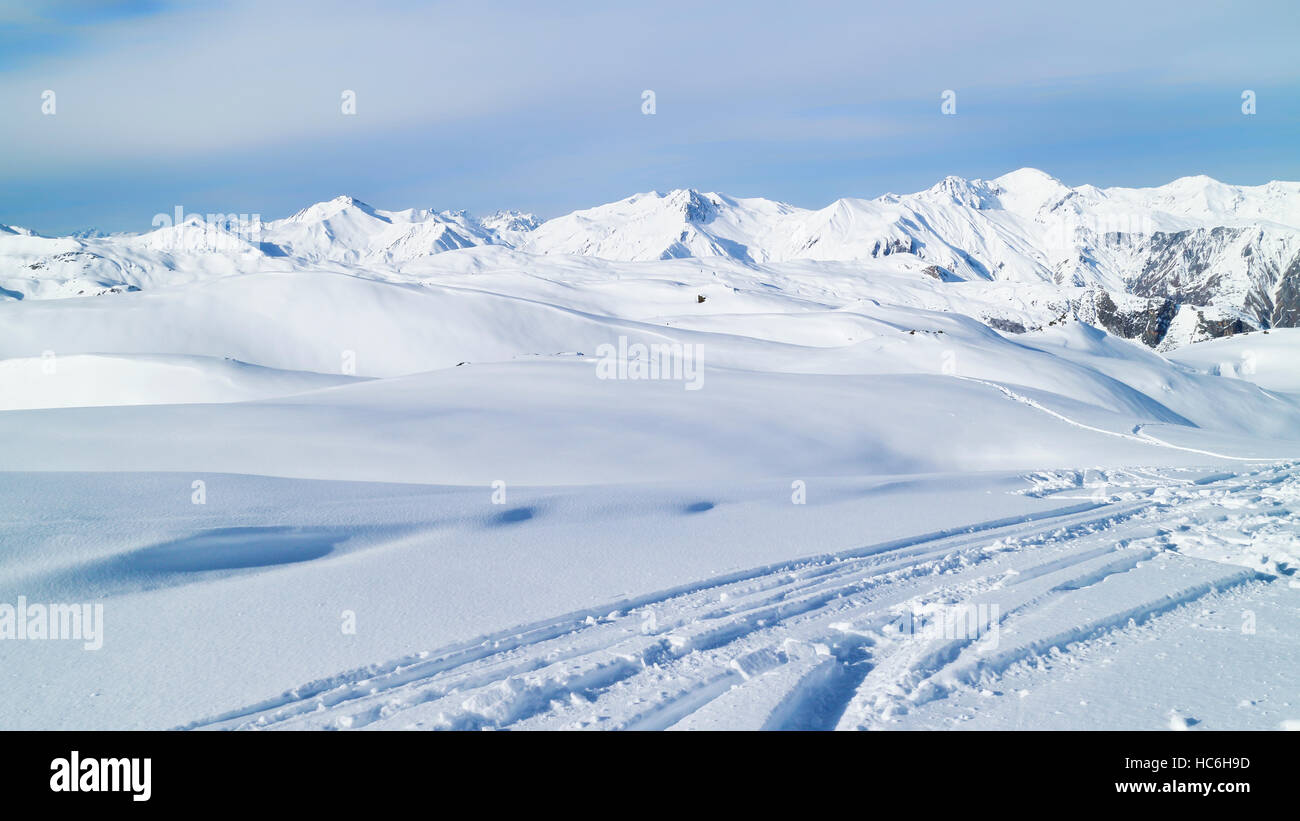 ski tracks on fresh snow in mountains with alpine peaks in the background. Winter snowy peaks landscape. Stock Photo