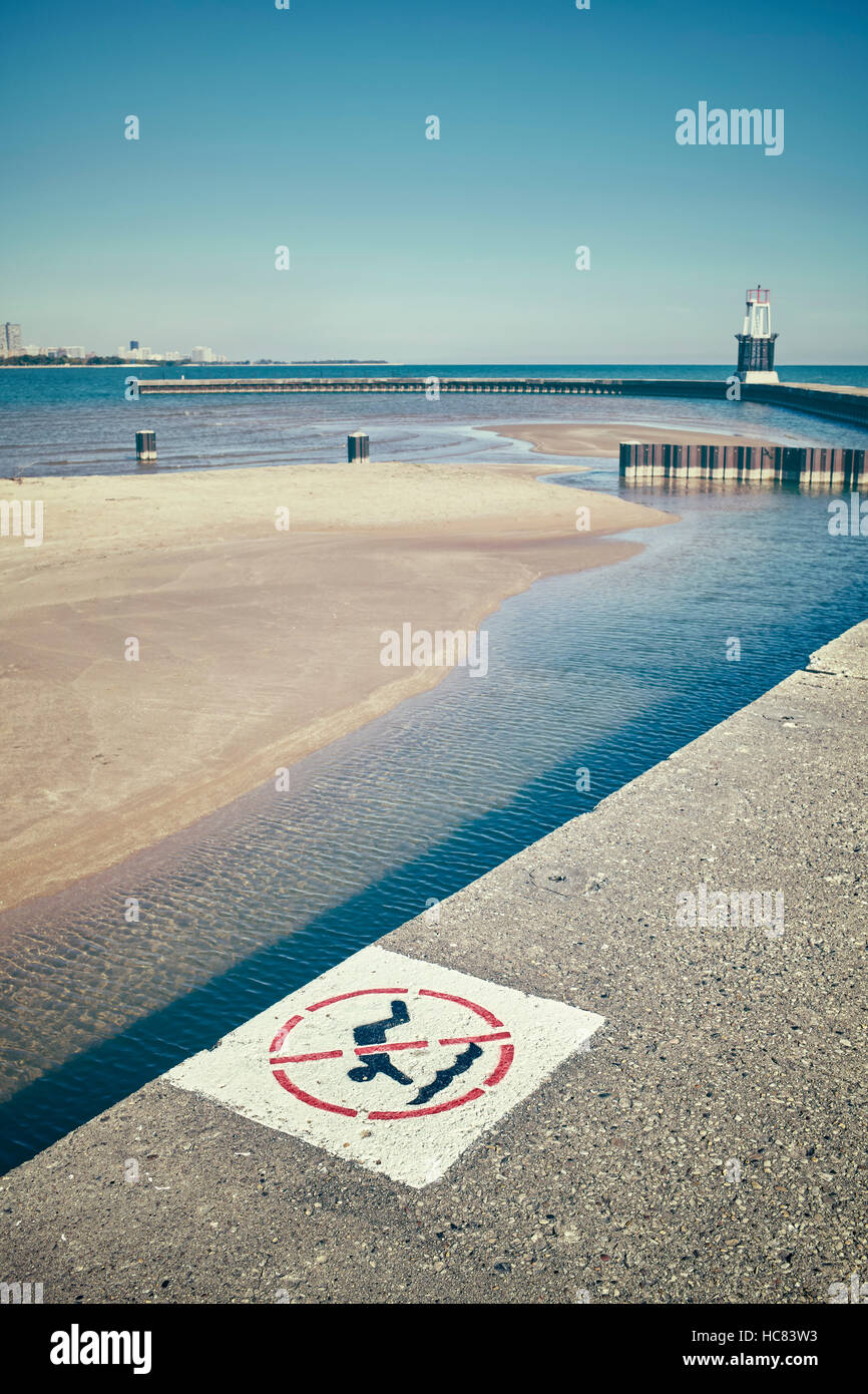 Retro stylized no diving sign on a pier with shallow water in background, selective focus on painted sign. Stock Photo