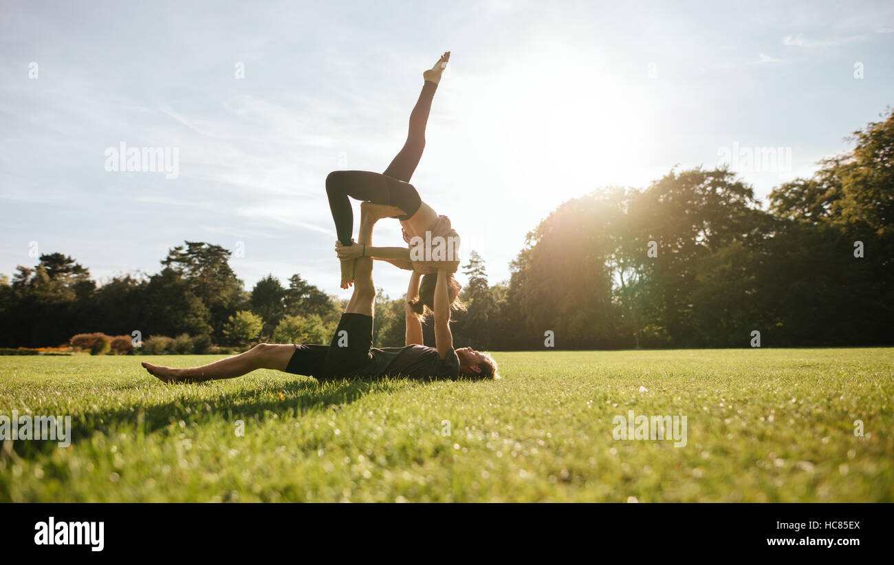 Strong young couple doing acroyoga workout. Man and woman in park practising pair yoga in morning. Stock Photo