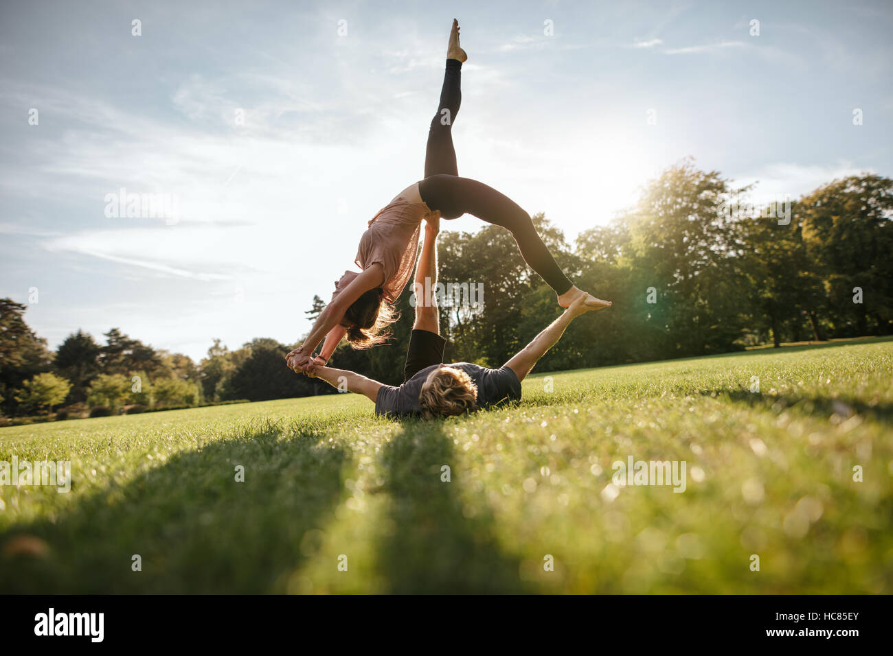 Outdoor shot of young man and woman doing yoga in pair. Couple doing acrobatic yoga exercise at park. Stock Photo