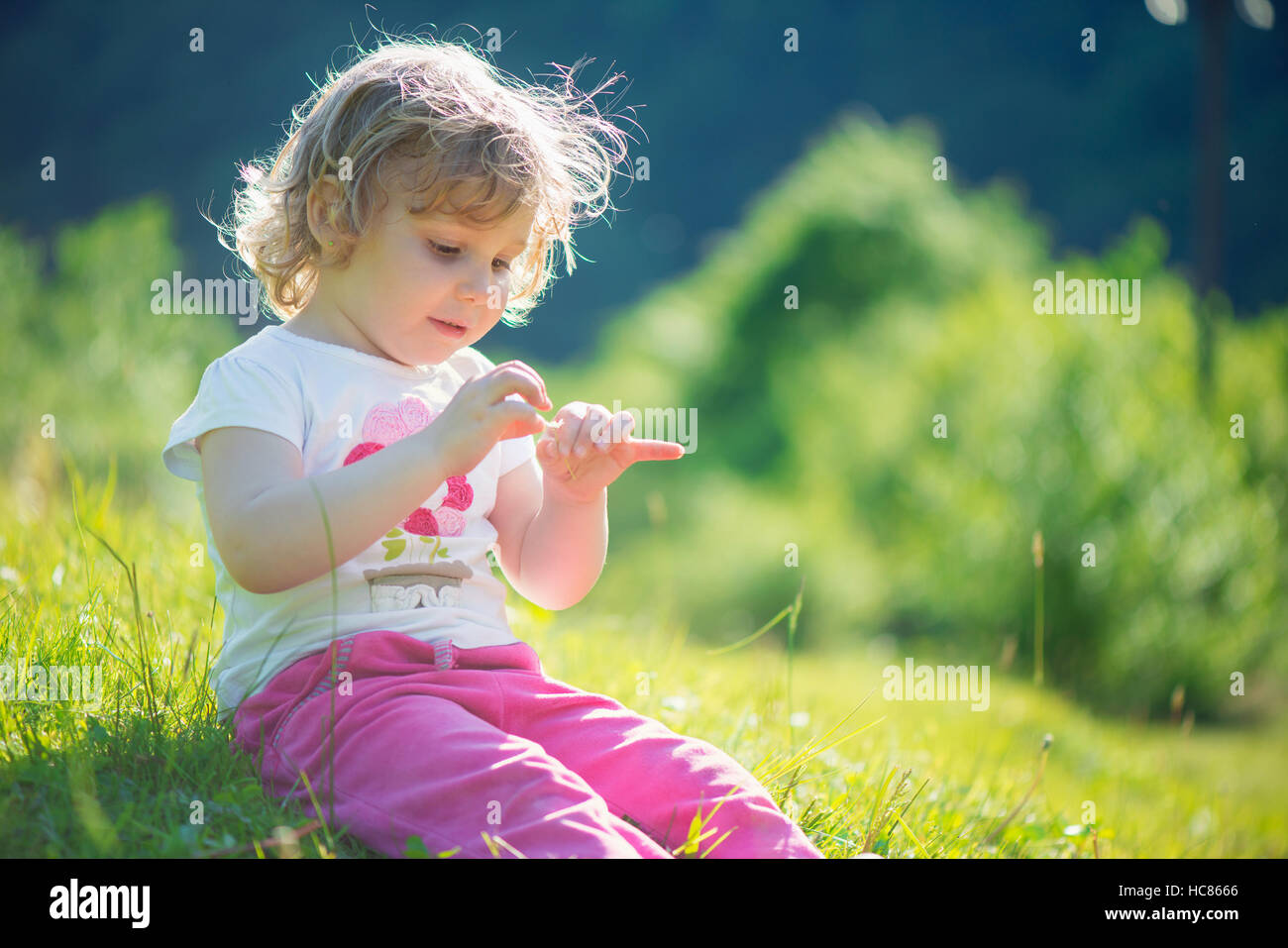 Cute little girl playing at sunny green meadow Stock Photo - Alamy