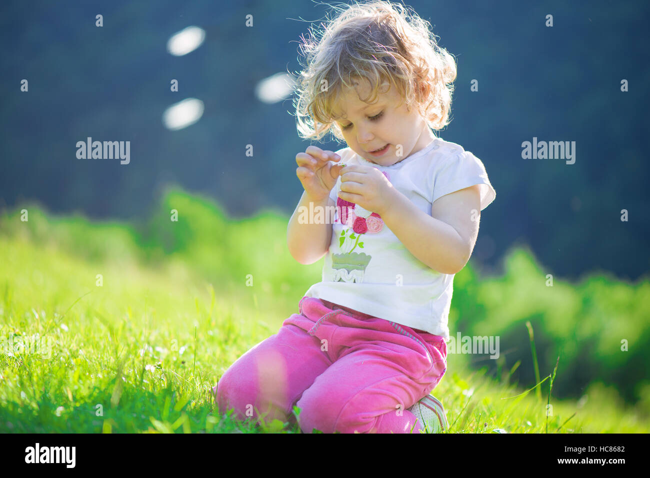 Cute little girl playing at sunny green meadow Stock Photo - Alamy