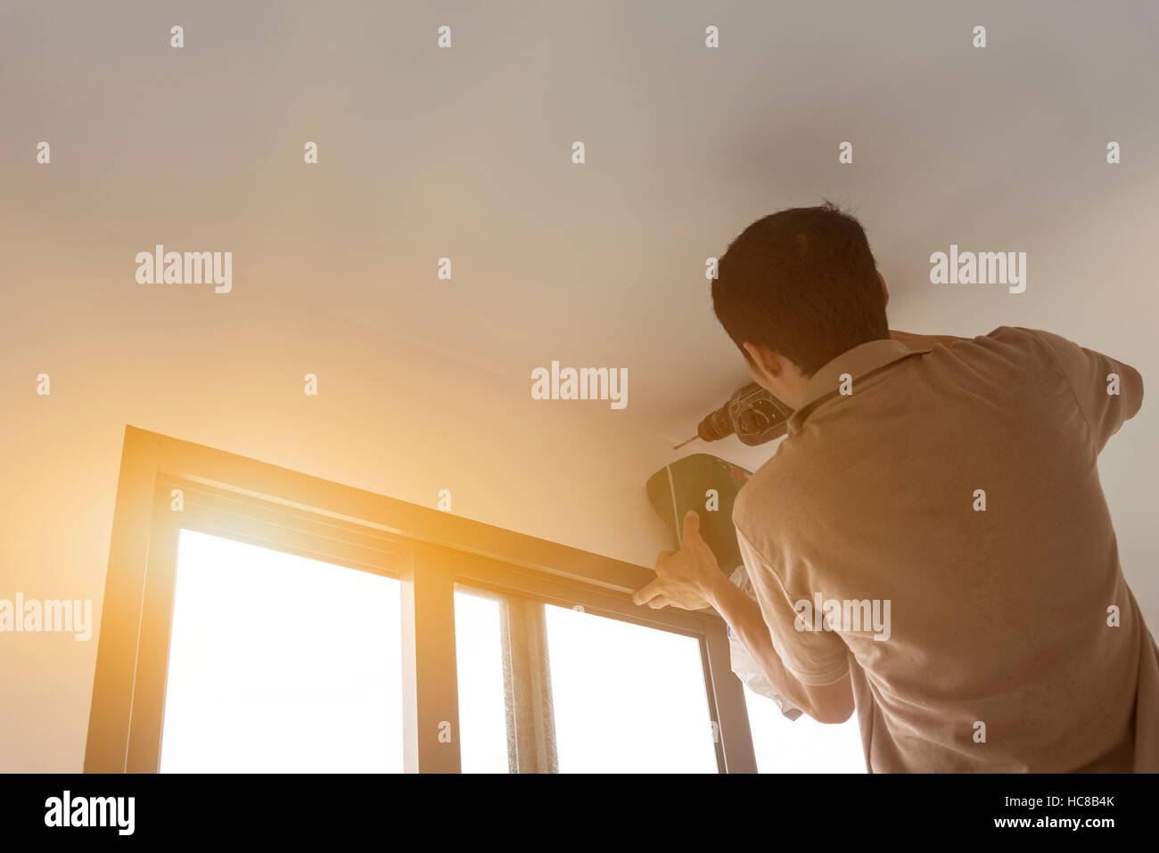 construction worker builder during formwork installation drilling ceiling for curtain rail. Stock Photo