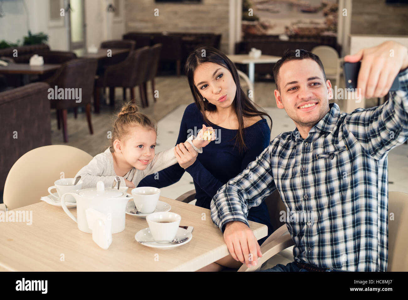 family, parenthood, technology people concept - happy mother, father and little girl having dinner taking selfie by smartphone at restaurant Stock Photo