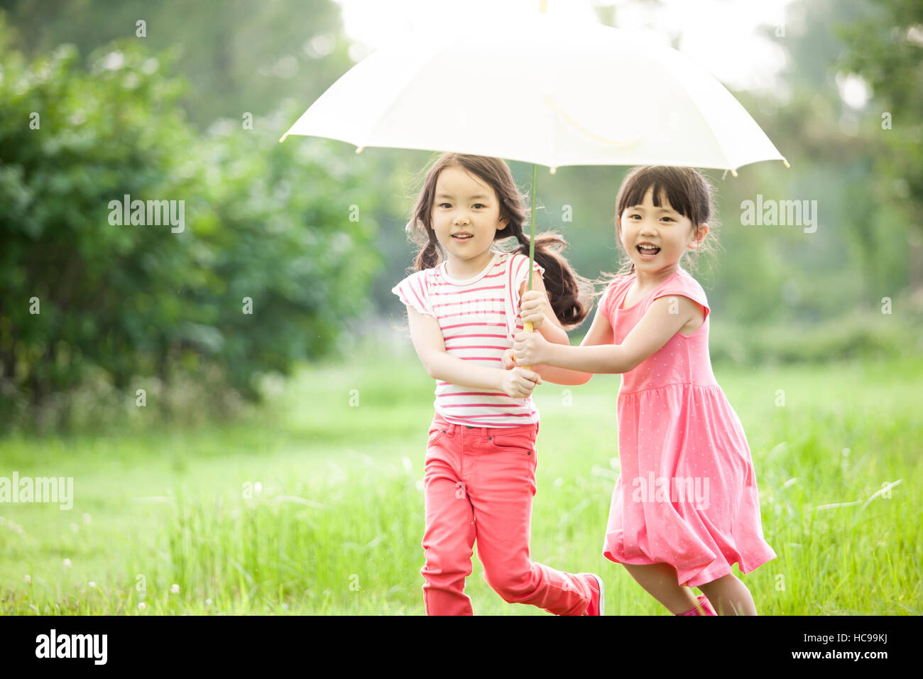Two smiling girls with an umbrella running in field Stock Photo - Alamy