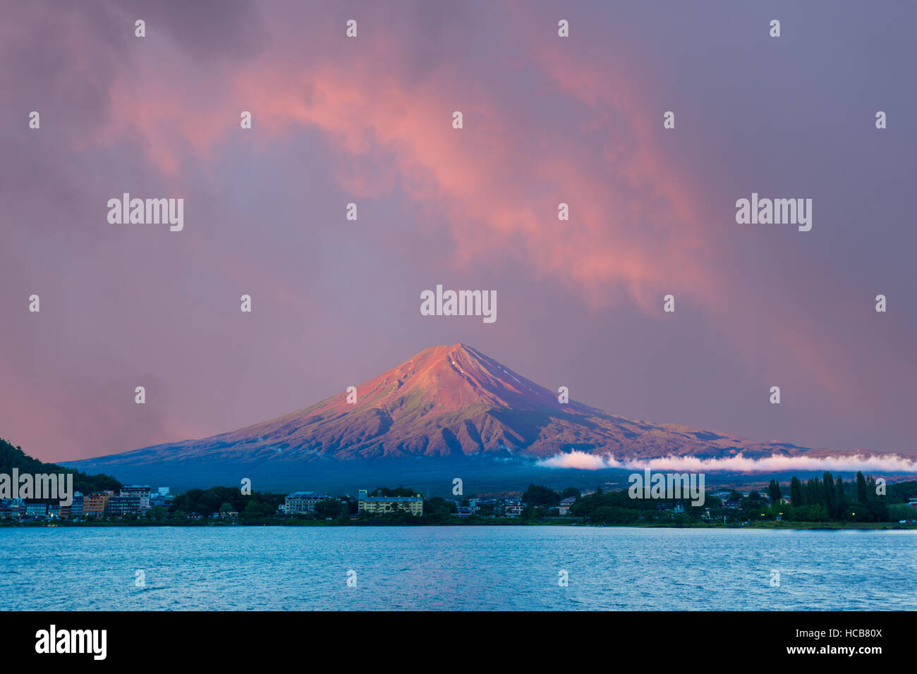 Colorful pink sunrise sky above the bright red volcanic cone of Mount Fuji with line of lake shore hotels in foreground during s Stock Photo