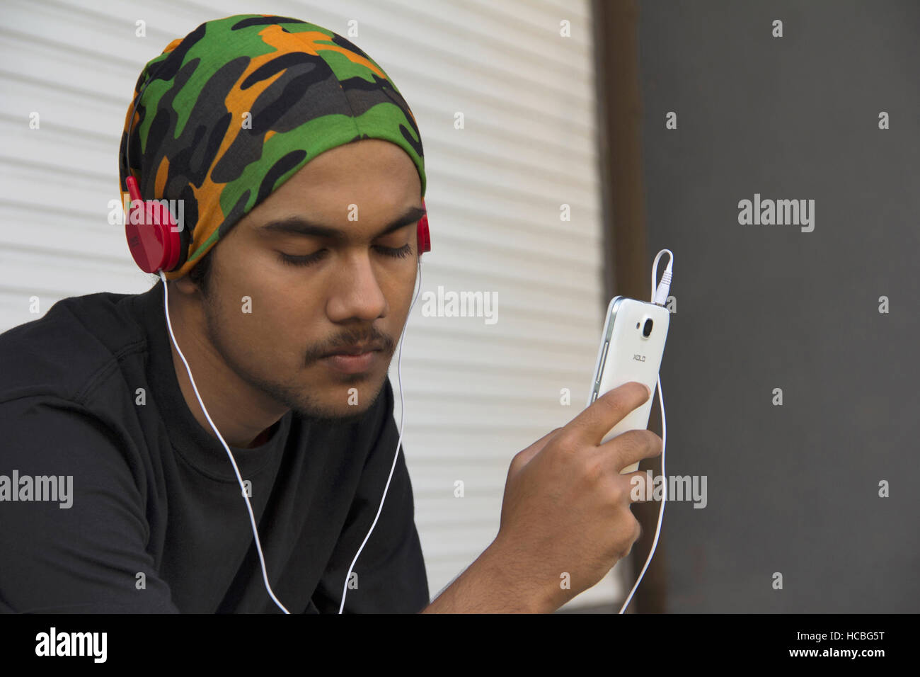 Close-up of a young Indian boy sitting and enjoying music on cell phone Stock Photo