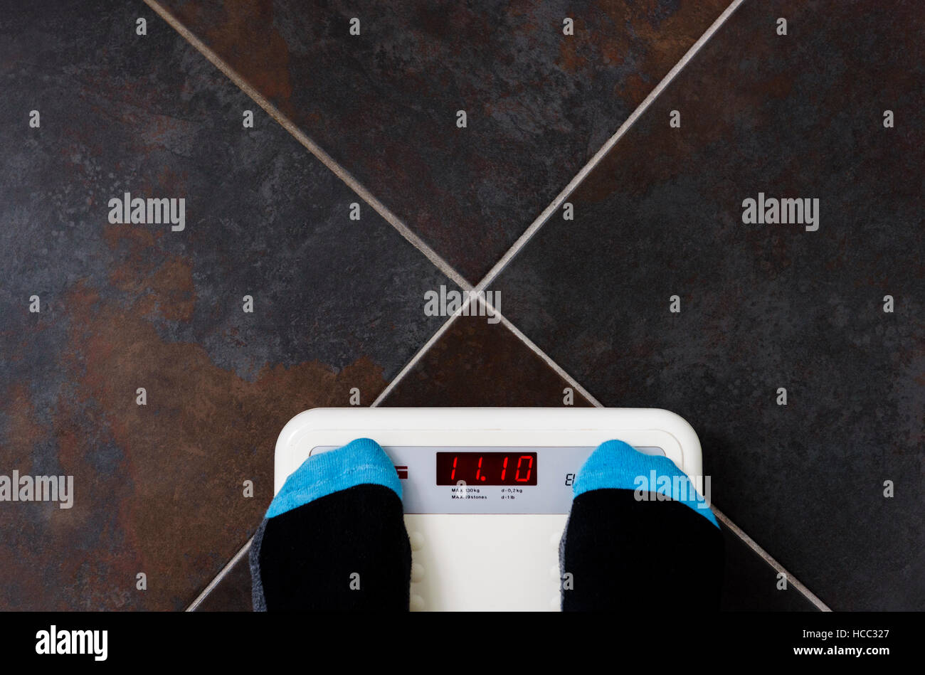 Bathroom scales on tiled floor with man wearing socks. Stock Photo