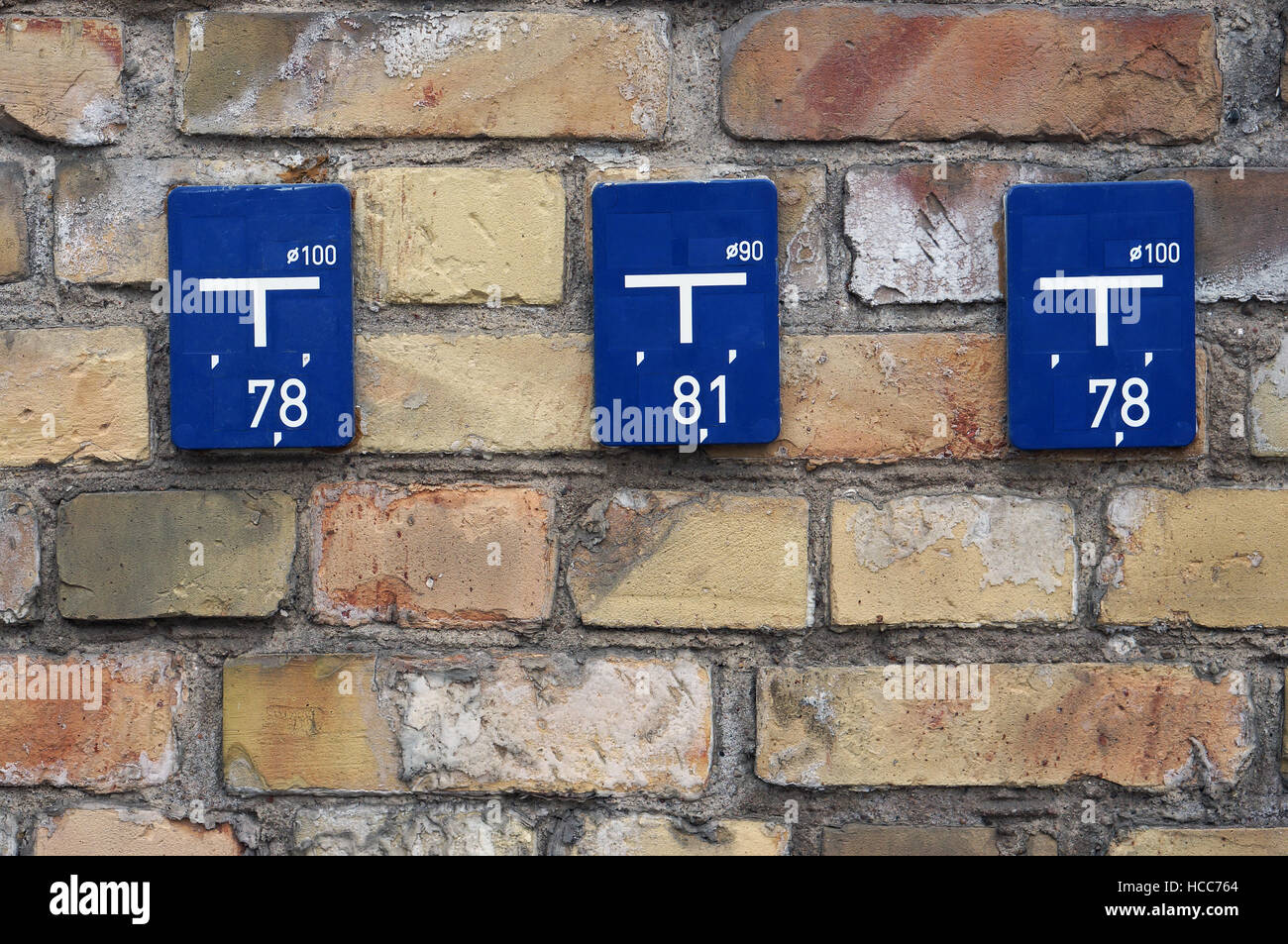 On a brick city wall blue information plates with information on coordinates of water pipes are located Stock Photo