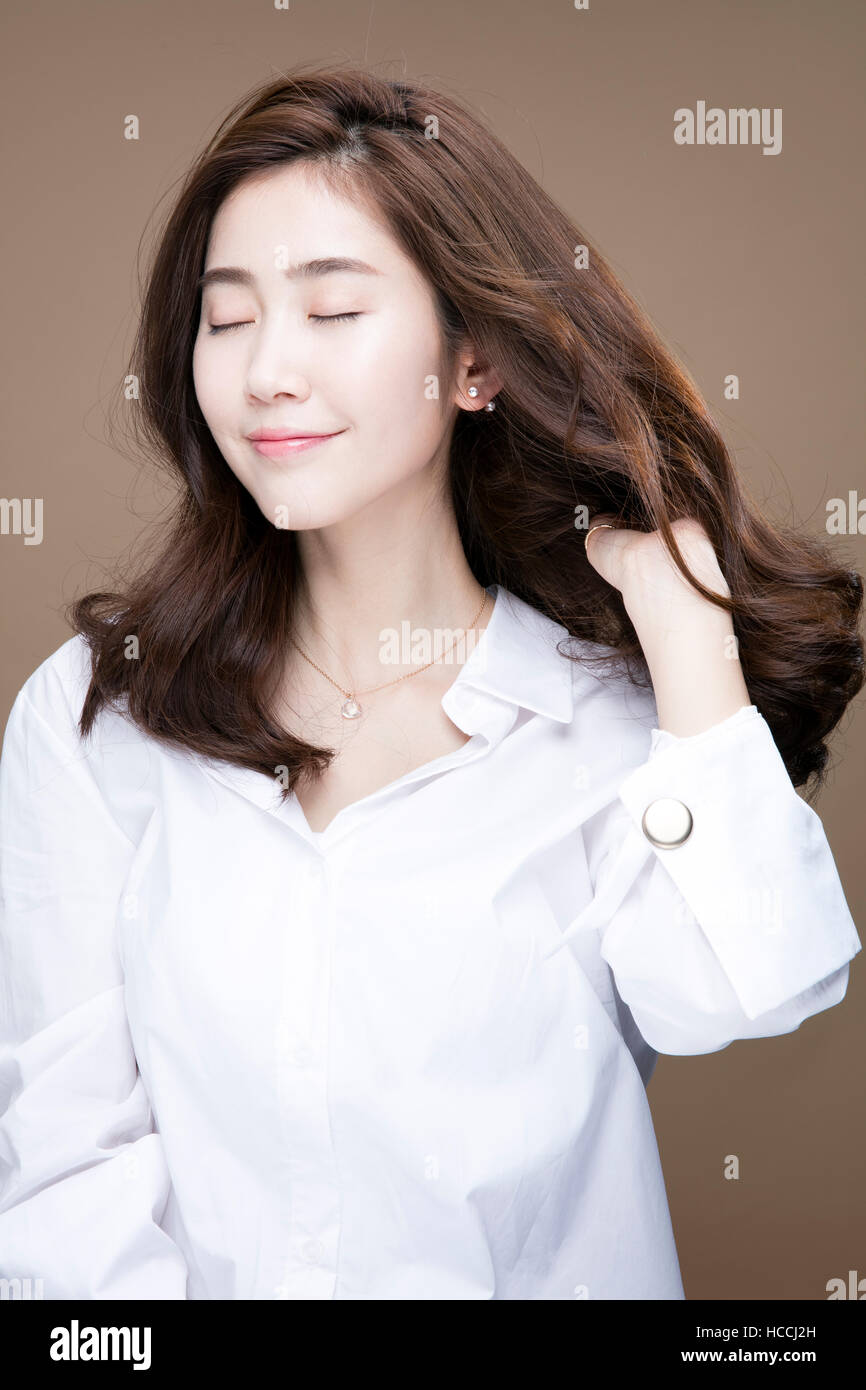 Portrait of young smiling woman with long wavy hair in white shirt ...