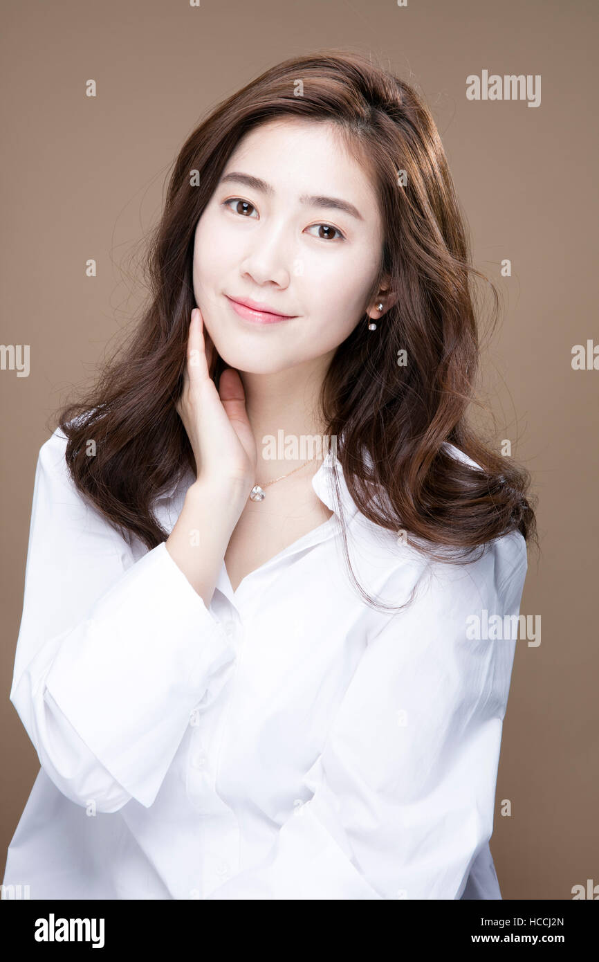 Portrait of young smiling woman with long wavy hair in white shirt ...