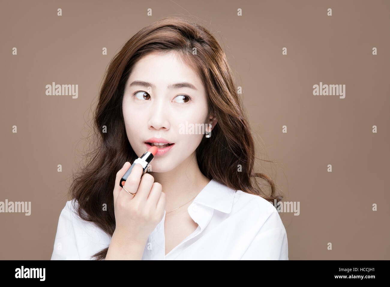 Portrait of young woman putting on lipstick Stock Photo