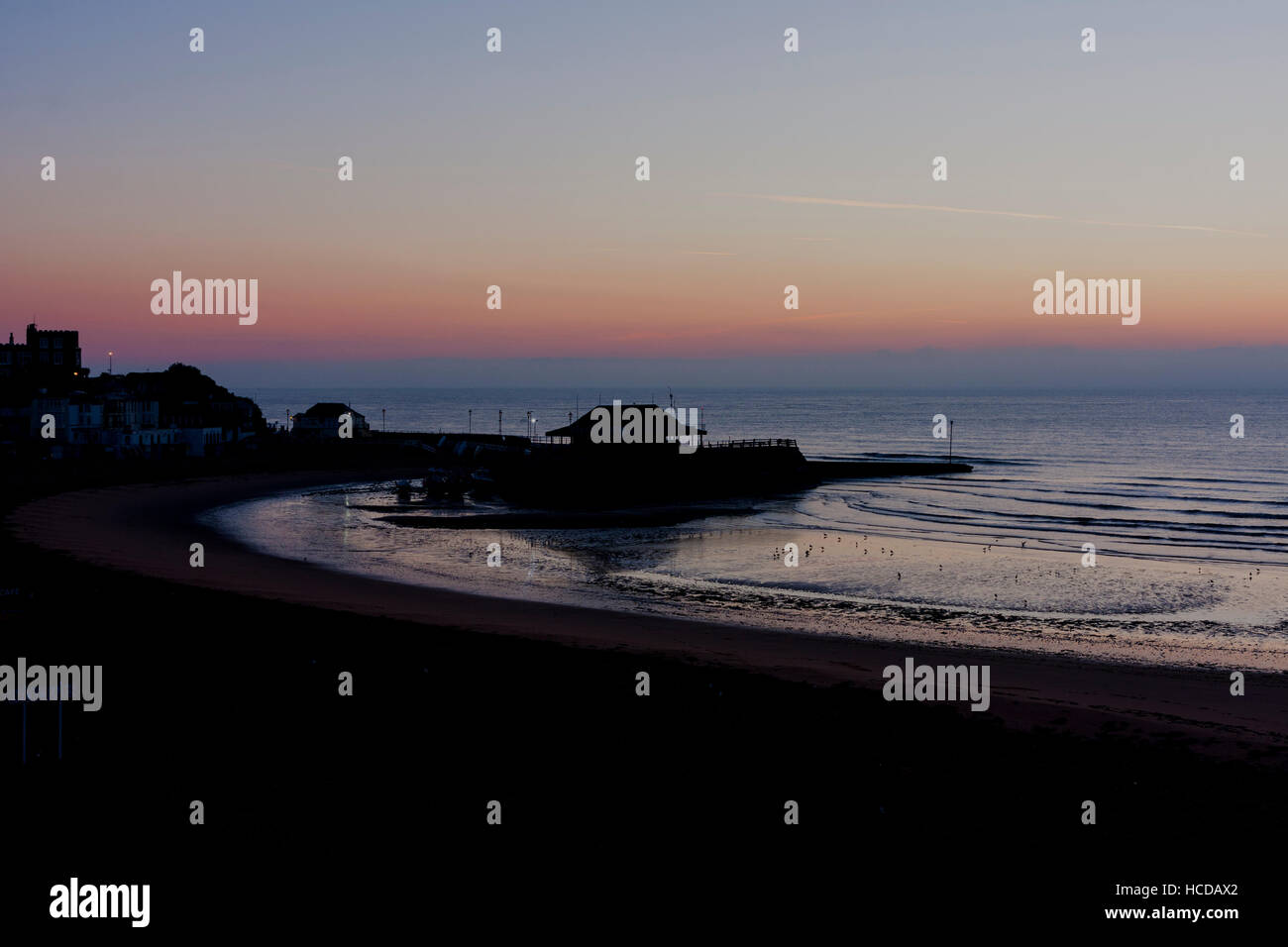 Dawn sky breaking over the sea at Broadstairs with the harbour and beach in the foreground. Clear sky with cloud layer on horizon. Calm sea. Stock Photo