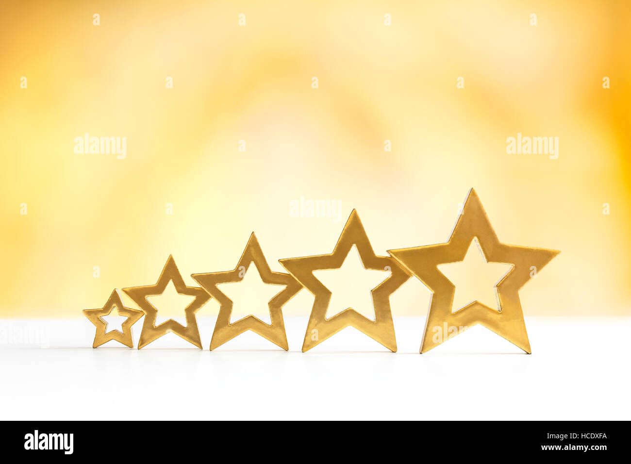 Five golden shining stars in ascending order on white and yellow background, flames, fire, copy space Stock Photo