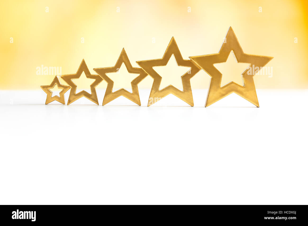 Five golden shining stars in ascending order on white and yellow background, copy  or text space, sign for perfect service Stock Photo