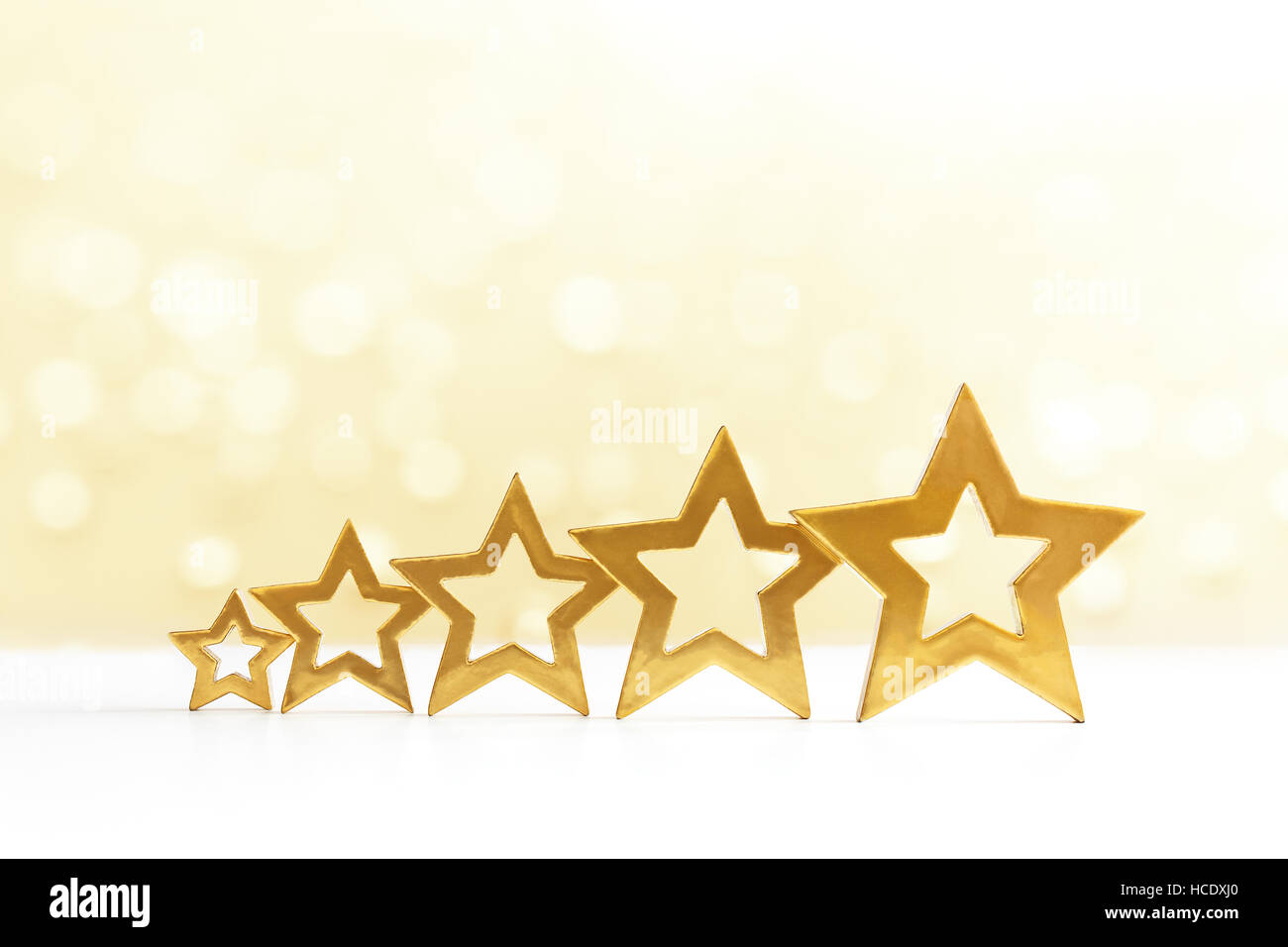 Five golden shining stars in ascending order on white and yellow sparkling background, copy space Stock Photo