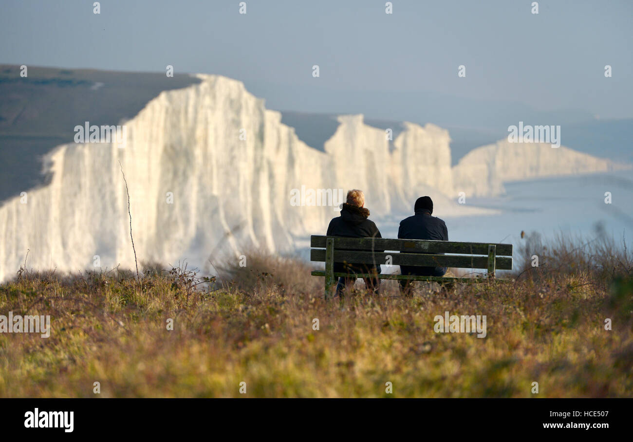 Seven Sisters, East Sussex. Two people sitting on a bench looking at the Seven Sisters chalk cliffs in the South Downs National Stock Photo