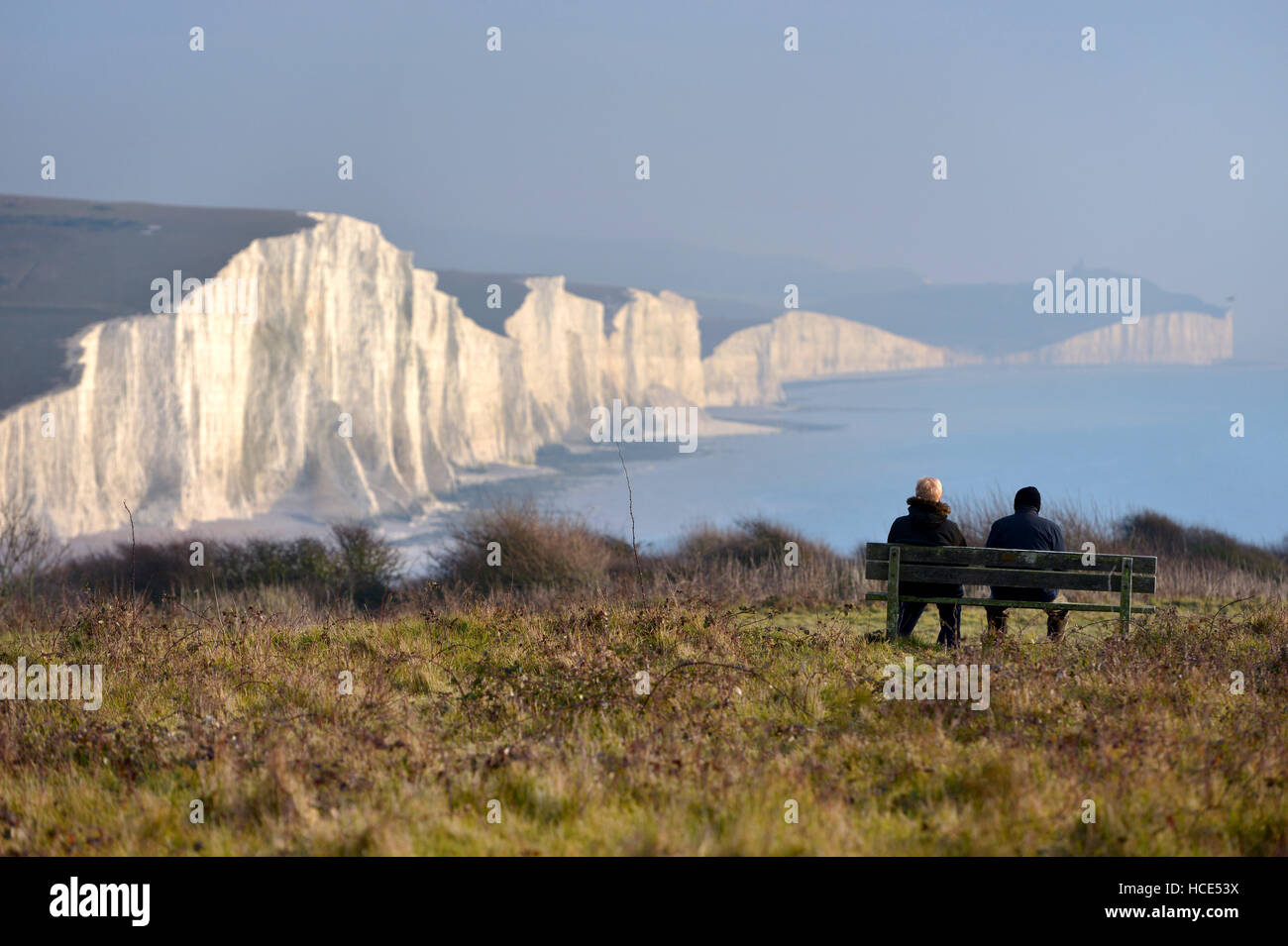 Seven Sisters, East Sussex. Two people sitting on a bench looking at the Seven Sisters chalk cliffs in the South Downs National Stock Photo