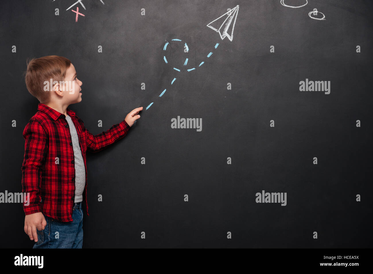 Cute little boy dressed in shirt in a cage looking at arrow drawn on chalkboard and pointing on it. Stock Photo
