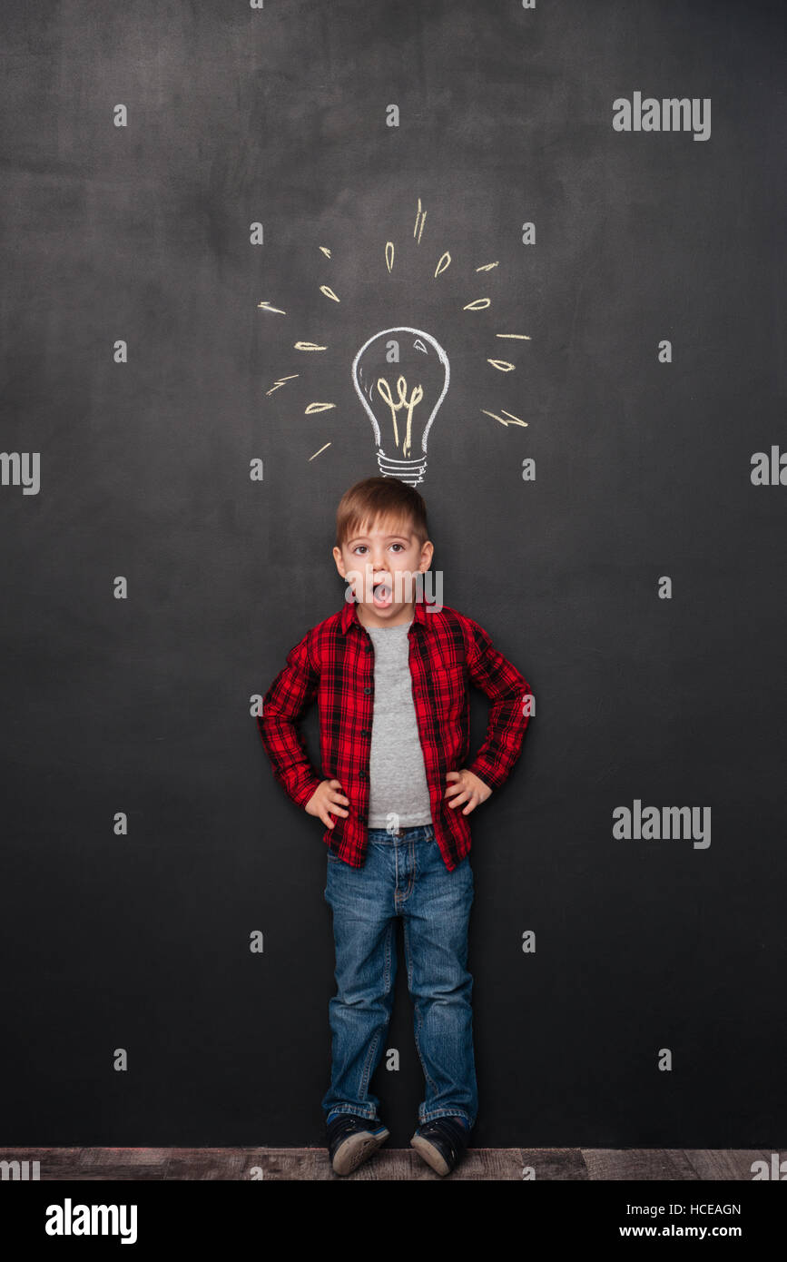 Picture of a little surprised boy having an idea over chalkboard background with drawings. Look aside. Stock Photo