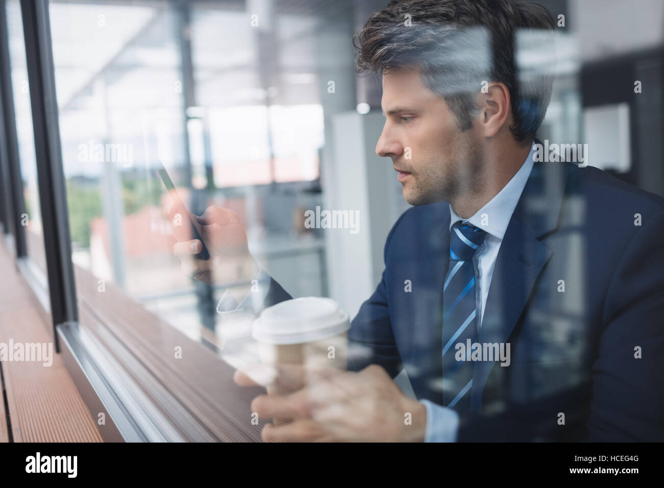 Businessman using mobile phone and holding disposable coffee cup Stock Photo