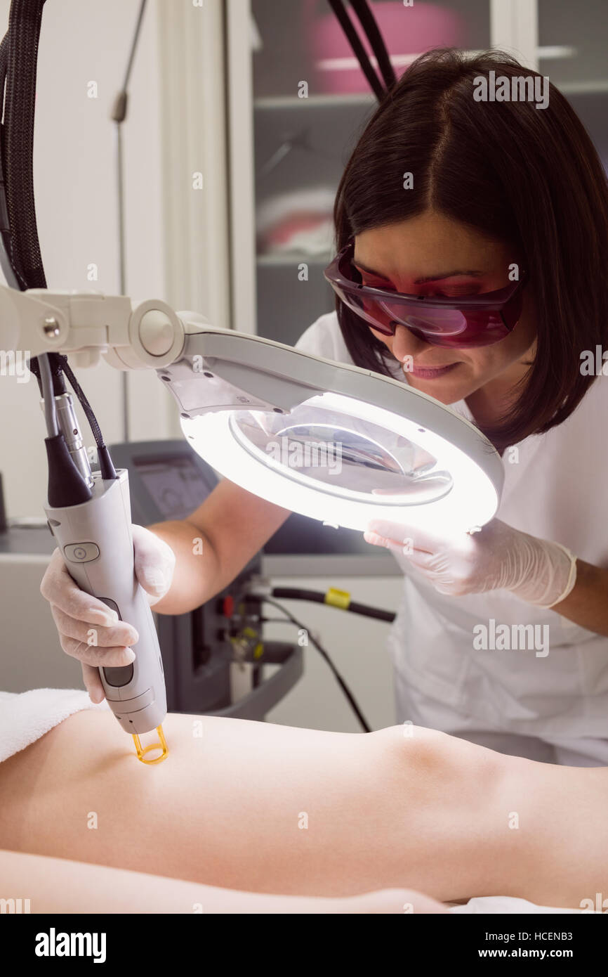 Doctor performing laser hair removal on female patient skin in clinic Stock Photo