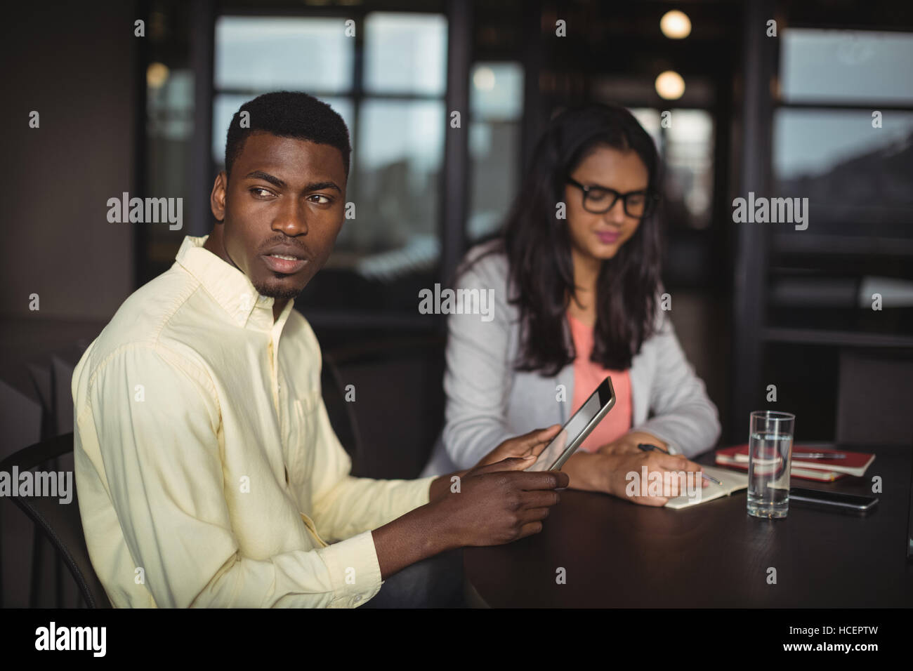 Businessman holding digital tablet while colleague writing notes Stock Photo
