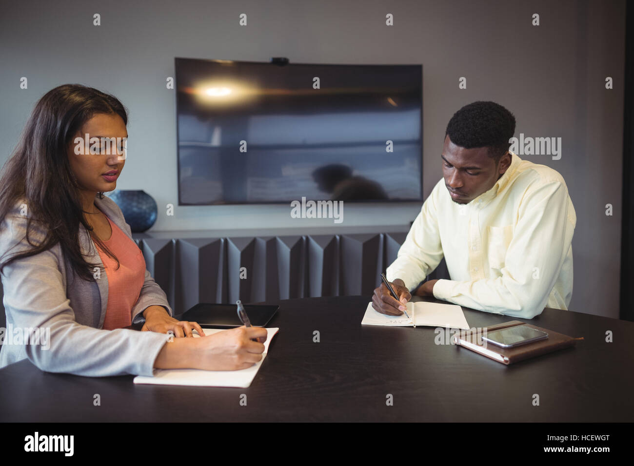 Businesswoman and colleague writing in a diary in conference room Stock Photo
