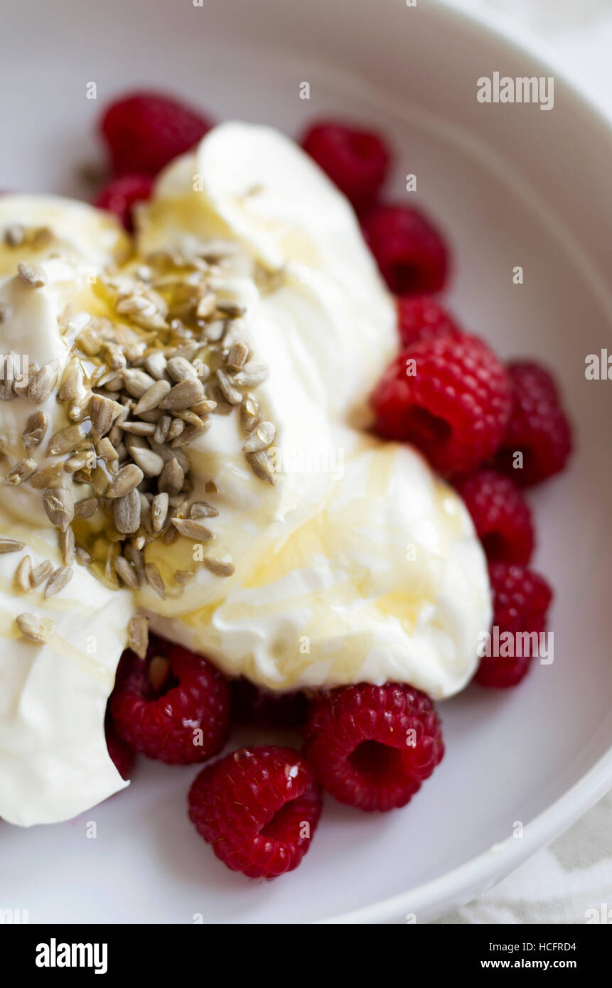 Fresh raspberries served with Greek yogurt, honey and sunflower seeds in a white bowl Stock Photo
