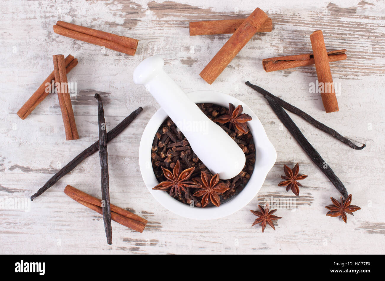 Fragrant cloves in white glass mortar and spices on rustic wooden board ...