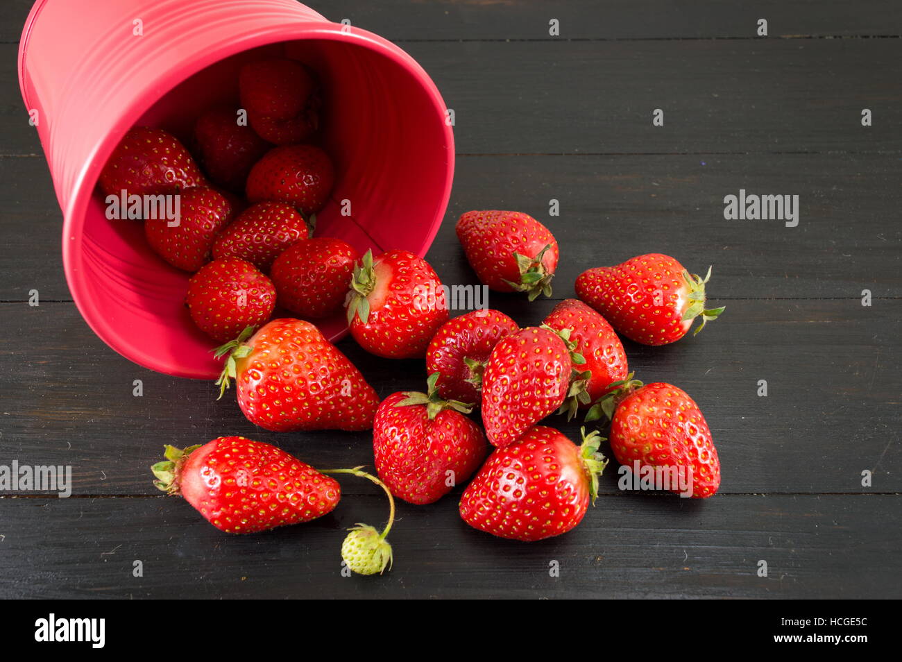 strawberries falling out of a red bucket on a black table Stock Photo